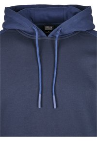 Felpa con cappuccio di colore blu navy, realizzata in un tessuto morbido. Presenta lacci abbinati e orlo a costine. Etichette visibili all'interno del colletto.