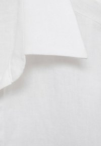 Gros plan d’un col de chemise blanc et net en tissu léger texturé, montrant des coutures propres et des bords nets.