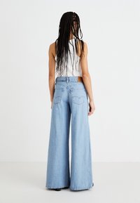 Světle modré džínové kalhoty s širokými nohavicemi, vyrobené z denimu, se zvýšeným pasem, pětikusovým designem a hnědou koženou visačkou na zadním pásku.