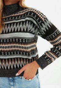 Schwarzer Strickpullover mit hohem Kragen, der geometrische Muster in Grau, Braun und Weiß aufweist. Strukturierte Bündchen und Saum.