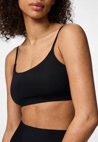 Il bralette nero presenta spalline sottili e regolabili, una texture liscia e un design senza cuciture, offrendo una vestibilità minimalista e confortevole.