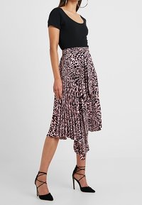 Černý top s výstřihem do véčka spárovaný s růžovou midi sukní s potiskem zvířecího vzoru, která má design do zavinování, sklady a volný střih. Černé jehlové podpatky.