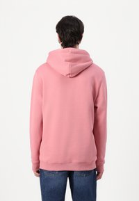 Felpa in cotone rosa con un ampio cappuccio, polsini e vita a coste, vista da dietro, abbinata a jeans blu.