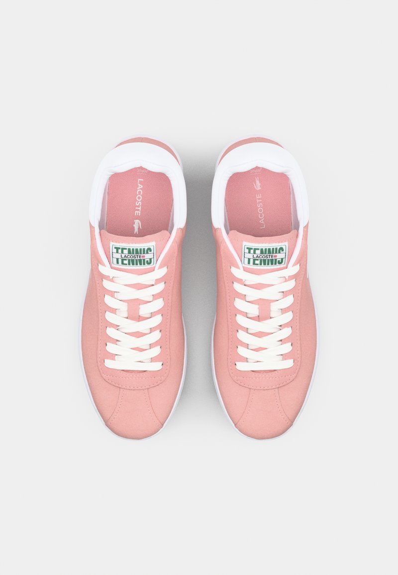 Zapatillas de tela rosa con suelas de goma blancas, cordones blancos y etiquetas verdes que dicen "LACOSTE" y "TENNIS". Punta redondeada y cuello acolchado.