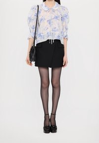 Bluzka w kwiatowy wzór w jasnym niebieskim i białym kolorze, z bufkami i kołnierzykiem. Czarna spódnica z zakładką, przejrzyste czarne rajstopy oraz czarne buty na obcasie.