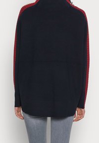 Pull marine avec panneaux latéraux rouges texturés, encolure ronde et bordures côtelées. Le vêtement présente une coupe décontractée et des manches longues.