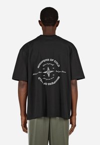 Μαύρη βαμβακερή μπλούζα με κοντό μανίκι και στρογγυλή γραφική απεικόνιση στην πλάτη, που περιλαμβάνει το κείμ�ενο "ΨΙΘΥΡΟΙ ΤΟΥ ΚΡΥΟΥ" και ένα σχέδιο πυξίδας σε λευκό χρώμα.