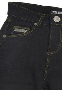 Schwarze Denim-Jeans mit gelben Nähten, ausgestattet mit einer Vordertasche, einem "TROUBLEMAKER"-Label und einem Metallknopfverschluss.