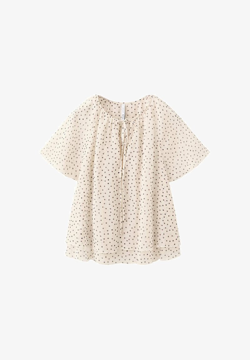 Blouse crème à manches courtes avec pois noirs, encolure ronde et détail noué devant, coupe ample, tissu léger.