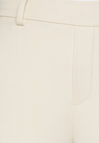 Beżowe, dopasowane spodnie o gładkiej teksturze, z kieszenią boczną oraz starannym wykończeniem wzdłuż pasa i krawędzi kieszeni.