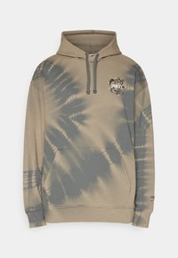 Sweat à capuche marron clair avec un motif tie-dye dans des teintes plus sombres. Il dispose d'une poche kangourou, d'une capuche avec cordon de serrage et d'un petit logo sur la poitrine.