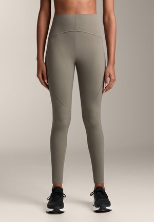 Hoge taille, olijfgroene leggings van rekbaar materiaal, met zijnaad voor contourvorming en gecombineerd met zwarte sportschoenen.
