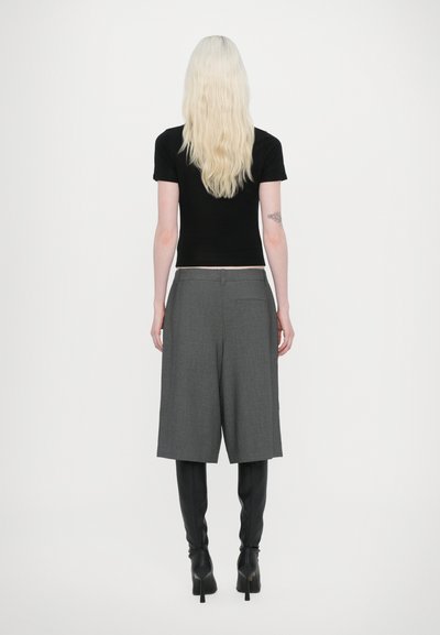 Haut ajusté à manches courtes noir associé à un short taillé gris, longueur genoux. Le mannequin porte des bottes à talons hauts noires. Vue de dos.