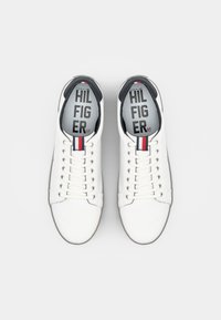 Ett par vita lädersneakers med vita snören, svart innertyg och röda, vita och blå dragflikar, sedd ovanifrån.