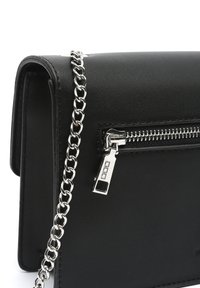 Sac à main en cuir noir avec un design à rabat, doté d'une bandoulière en chaîne argentée et d'une poche zippée à l'avant avec des détails en métal.