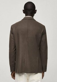 Sacou maro, croit, cu o țesătură fină, umeri structurați, vent singular și manșete cu nasturi. Design minimalistic fără embellishments.