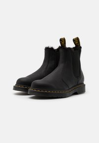 Botas Chelsea de cuero negro con paneles laterales elásticos, forro de piel de oveja y costuras amarillas en la suela. Cuenta con tiradores para facilitar su uso.