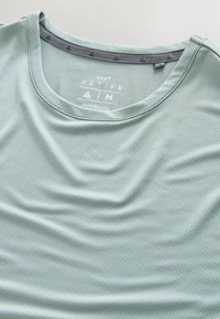 Hellgrünes aktives T-Shirt aus strukturiertem Stoff, mit Rundhalsausschnitt und einem dreieckigen Muster entlang des Kragens.