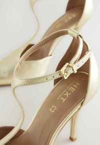 Guld högklackade sandaler med en elegant design, med en glänsande läderfinish, ankelrem med ett guldspänne och en spetsig tå.