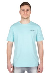 Camiseta de algodón azul claro con cuello redondo y mangas cortas. Presenta texto impreso en el lado izquierdo del pecho: "Amigos Equivocados: Viaje por Ibiza."
