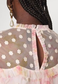 Gennemsigtig bluse med blomsterbroderi, pastelfarvet skema, flæset halsudskæring, knaplukning bagpå og en struktureret stof.