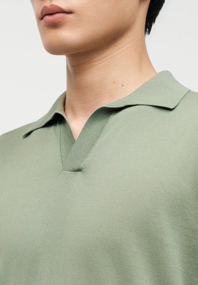 Ανοιχτό πράσινο κοντομάνικο πόλο πουκάμισο με σχεδίαση V-λαιμού και έναν λείο, υφασμάτινο υλικό με υφή. Διαθέτει διακριτικό γιακά και καθαρές γραμμές.