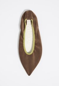 Zapato plano de tela marrón con punta afilada, ribete elástico verde alrededor de la abertura y un forro interior suave. Textura lisa sin hardware visible.