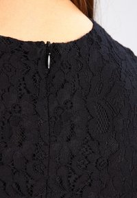 Svart spetsekjol med texturerade blommönster, med en diskret dragkedja bak. Tyget har en delikat, intrikat design.