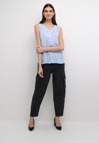 Top sin mangas de color azul claro con un patrón floral, combinado con pantalones cargo negros. El conjunto se complementa con unos tacones negros de punta.