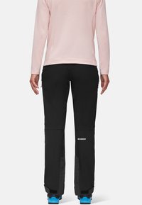 Czarne spodnie outdoorowe z regulowanymi mankietami, płaskimi szwami i kieszeniami na zamek. Noszone z różową bluzką z długim rękawem, z teksturowanej tkaniny.