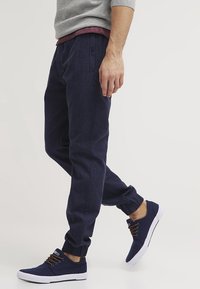 Marine joggings met een gestructureerde afwerking en elastische boorden, gecombineerd met marine sneakers met bruine veters en een witte zool.