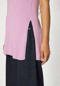 Top de malha pink canelado com fendas laterais, combinado com denim escuro. O tecido apresenta uma textura suave e uma forma justa ao redor do torso.