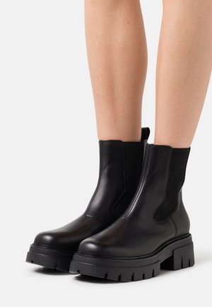 Schwarze Leder-Stiefeletten mit seitlichen elastischen Einsätzen, dicken Gummisohlen, abgerundeten Zehen und minimalen Nähdetails.