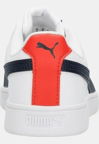 Sneaker bianca con dettagli rossi e blu navy, tomaia in sintetico testurizzato, tallone imbottito e logo marchiato sul retro. Design della suola piatta.