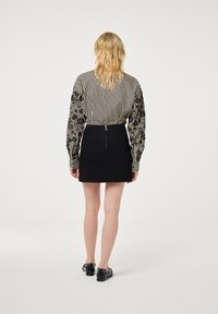 Zwarte denimrok met een getailleerd ontwerp, gecombineerd met een gestreepte blouse met poffende mouwen en ingewikkelde zwarte accenten.