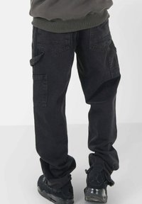 Svarta cargobyxor med flera fickor, lös passform, fransigt avslut och slitstarkt bommaterial. Matchas med svarta sportskor.