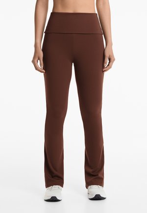 Braune Sportleggings mit einem hohen, gefalteten Bund, glatter Textur und maßgeschneidertem Schnitt, der am Knöchel leicht ausgestellt ist.