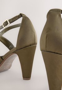 Rohelised satiinist kõrged sandaalid pahkluupaelaga, millel on tekstuurse viimistlusega ja massiivse plokksandaali kontsaga disain.