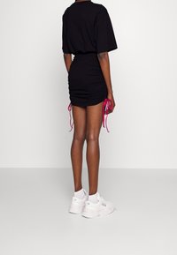 Zwarte T-shirt jurk met geplooid ontwerp en roze trekkoorden aan de zoom. Gecombineerd met witte sneakers. Gladde stof, casual pasvorm.