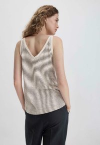 Gestreepte tanktop in crème en bruin, met een V-hals en een relaxte pasvorm, gecombineerd met donkere broeken. Effen stof met subtiele textuur.