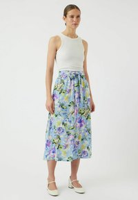 Blommig maxiklänning i ljusblått med lila och gröna mönster, med knyt i midjan och flödande tyg. Matchas med en vit ärmlös topp.