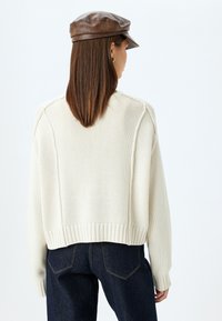 Maglione a maglia crema con un design corto, cuciture testurizzate e orlo a coste, abbinato a jeans a vita alta blu scuro.
