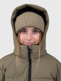 Jovem a usar um gorro de malha bege e uma jaqueta de inverno com capuz verde-oliva fechada, em frente a um fundo simples.