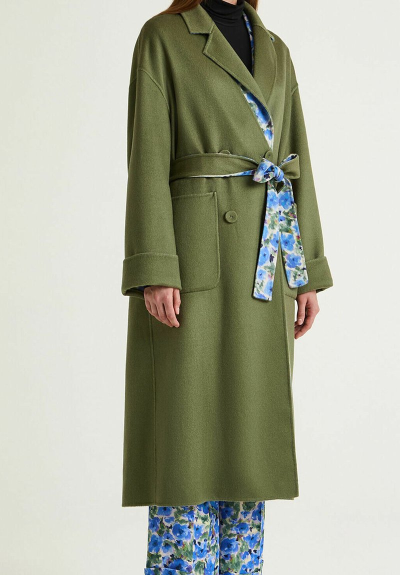 Manteau long vert olive avec ceinture nouée, doublure à motif floral et deux poches avant. Texture douce, coupe ajustée.