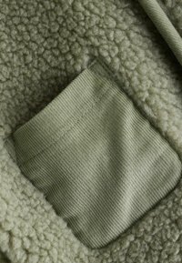 Fleece jacket featuring a soft, textured green body and a flat corduroy pocket in a slightly darker green shade.