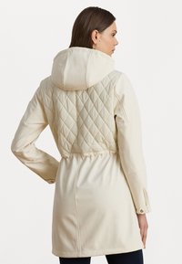 Light beige jacket with a diamond quilted back, hood, and elastic waist. Made from smooth fabric, features long sleeves and button accents.