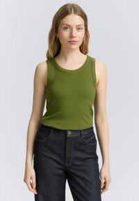 Grön ribbad linne med rund halsringning, figurnära passform och ärmlös design, parat med mörka denimjeans.
