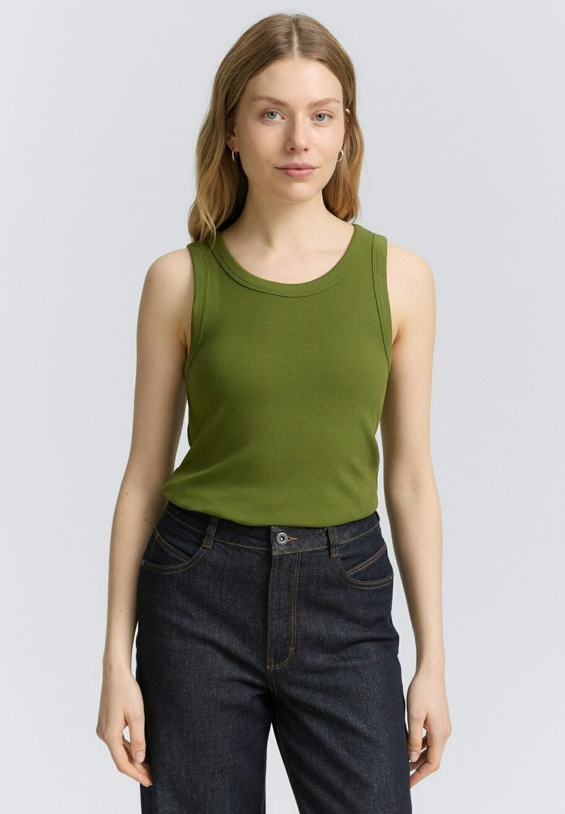 Grön ribbad linne med rund halsringning, figurnära passform och ärmlös design, parat med mörka denimjeans.