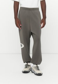 Grå sweatpants med elastisk talje, prydet med en hvid grafisk detalje. Bæres med lysegrå og sorte sneakers. Glat stofstruktur.