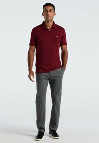 Bordeaux poloshirt met een kraag en korte mouwen, gecombineerd met een grijze broek en zwarte sneakers, met een klein logo op de borst.